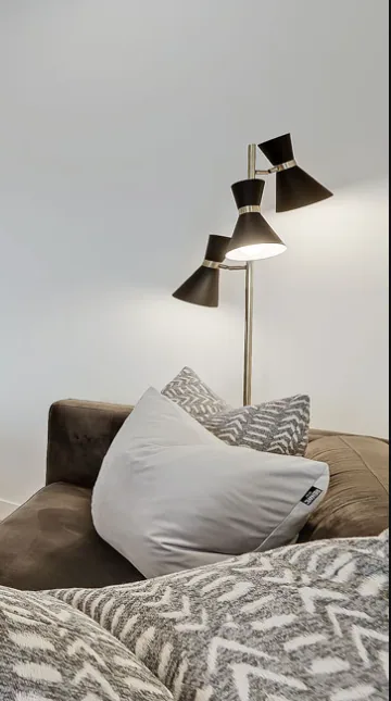 Editorial interior detail of a Renfrew multi-level home, black tri-cone floor lamp beside a brown velvet sofa with patterned cushions